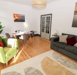 A living room with a green armchair, a gray sofa, a dining table with chairs, wooden floor and wall art at 36A Mary Street in Porthcawl