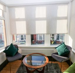 A sitting area with two chairs with green pillows and a round glass-top table near large windows at 36A Mary Street in Porthcawl