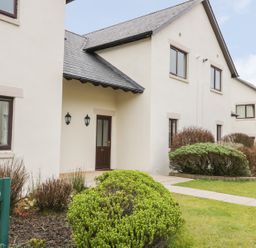 A white two-story house with a dark brown door and windows with bushes and a walkway in front at Whitbarrow 24 in Penruddock