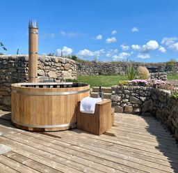 An outdoor wooden hot tub on a wooden deck with stone walls and garden plants at The Riblows Cape Cornwall Bollowal near St Just