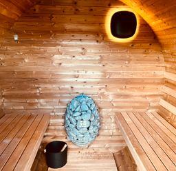 An interior of a sauna with wooden benches a heater with stones and a black bucket at The Riblows Cape Cornwall in Bollowal near St Just