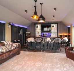 A lounge area with leather sofa and armchair with cushions and a bar with stools covered in fur at Glamorgan House Cardiff