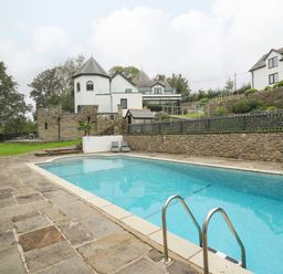 An outdoor swimming pool with stone patio and loungers near a white house with castle-like features and turrets at Glamorgan House in Cardiff