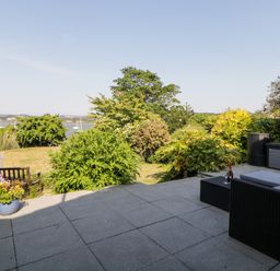 An outdoor patio with garden furniture and plants overlooking a body of water with sailboats at Riverview @ 1 Brunel View in Saltash
