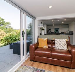 A living room with a brown leather sofa and sliding glass doors opening to a garden at Riverview @ 1 Brunel View Saltash
