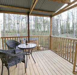 A wooden covered porch with two wicker chairs a glass top table with a bottle and glasses and a hot tub outside at The Leveret in Eppleby