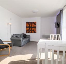 A living room with a gray sofa black armchair white dining table and chairs and wall art at Apartment 9 Beaconsfield House in Bridlington