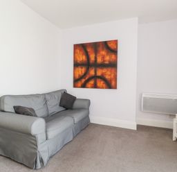 A living room with a grey sofa two dark cushions and an abstract wall art at Apartment 9 Beaconsfield House in Bridlington
