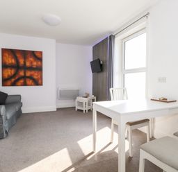 A living room with a gray sofa a white dining table and chairs a wall-mounted television and abstract paintings at Apartment 9 Beaconsfield House in Bridlington