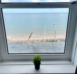 A window overlooking a beach and sea with a small potted plant on the windowsill at 7 Beach View @ Beaconsfield House Bridlington