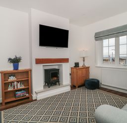 A living room with a TV above a fireplace and bookshelves by the walls at Quay Cottage Sea View in Poole