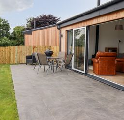 An outdoor patio with table and chairs next to a wooden building with sliding glass doors and brown leather chairs visible inside at 1 Orchard Cottages Dunstan near Craster