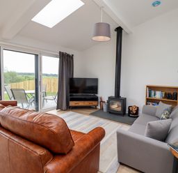 A living room with leather and fabric sofas a wood stove a television bookshelf and sliding doors to a patio at 1 Orchard Cottages Dunstan near Craster