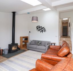 A living room with leather and fabric sofas a wood burning stove and a TV at 1 Orchard Cottages Dunstan near Craster