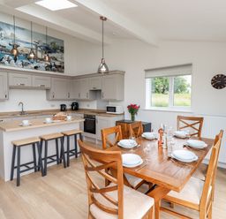 A kitchen with gray cabinets a wooden island with stools and a wooden dining table with chairs at 1 Orchard Cottages in Dunstan near Craster