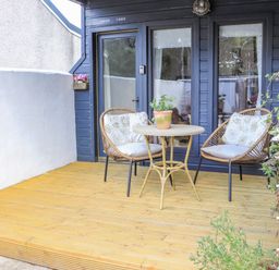 A wooden deck with two chairs and a round table with a potted plant in front of a cabin with blue walls and glass doors at Creed Cabin Stornoway