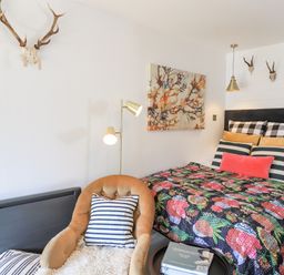 A bedroom with a bed decorated with patterned pillows and a floral quilt a chair with a striped pillow a floor lamp and skull decorations on walls at Creed Cabin in Stornoway