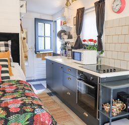 A small kitchen area with blue cabinets and a bed with colorful bedding and pillows at Creed Cabin in Stornoway