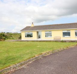 A single-story yellow house with a tiled roof and multiple windows on a grassy lawn with a paved driveway at Meeligolleen in Coill Tra