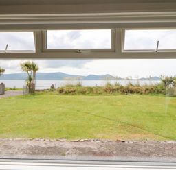 A large window view showing a lawn with palm trees and a body of water with mountains in the background at Meeligolleen in Coill Tra