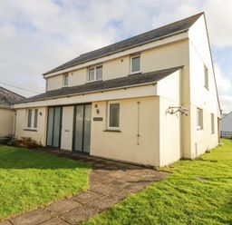 The exterior of a two-story cream-colored house with a paved walkway and grassy yard at Freefolk in Polzeath