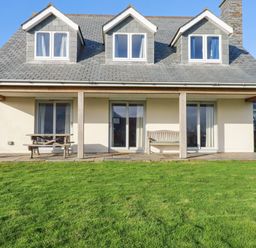 A house with three dormer windows a patio with a wooden bench and picnic table and a lawn in front at Freefolk in Polzeath