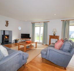A living room with two blue sofas a wooden coffee table a TV a wood burning stove and large windows at Freefolk in Polzeath