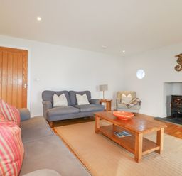 A living room with two gray sofas a wooden coffee table a small armchair a wood burning stove and a wooden door at Freefolk in Polzeath
