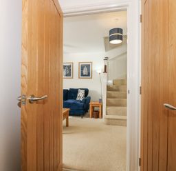 A living room with a blue sofa a wooden coffee table side table staircase and two framed pictures on the wall at The Mill Stones in Stalham