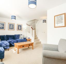 A living room with blue sofas wooden coffee table framed pictures and stairs at The Mill Stones in Stalham