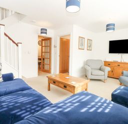 A living room with blue and gray chairs a wooden coffee table a wooden sideboard and a wall-mounted television at The Mill Stones in Stalham