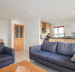 An open living room and kitchen with blue sofas a wooden door and light wood kitchen cabinets at Freefolk Cottage in Polzeath