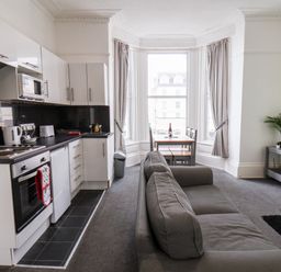 A kitchen and living area with white cabinets gray sofa dining table and large windows at Promenade in Bridlington