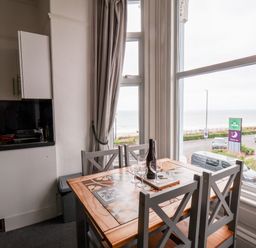 A dining table with four chairs near large windows overlooking a street and the sea at Promenade in Bridlington