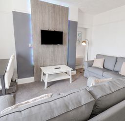 A living room with grey sofas a white coffee table a wall-mounted TV and a dining table with white chairs at Ocean Wave in Bridlington