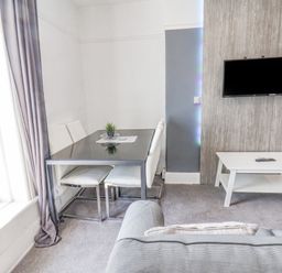 A dining area with a table and chairs next to a window and a wall-mounted TV above a coffee table at Ocean Wave in Bridlington