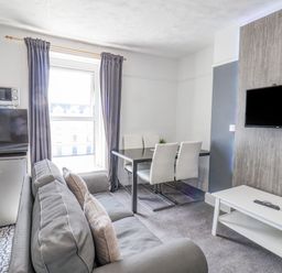 A living room with grey sofa, dining table with chairs, wall-mounted TV, and kitchen appliances at Ocean Wave in Bridlington