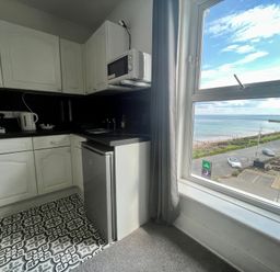 A small kitchen with white cabinets a mini fridge a microwave a kettle and a window overlooking a beach at Ocean Wave in Bridlington