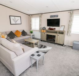 A living room with a sectional sofa, coffee table, television on a stand, and two windows with curtains at Beechwood Lodge in Hasguard Cross near Broad Haven