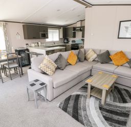 An open living room and kitchen with a corner sofa with cushions a coffee table and a dining table with chairs at Beechwood Lodge in Hasguard Cross near Broad Haven