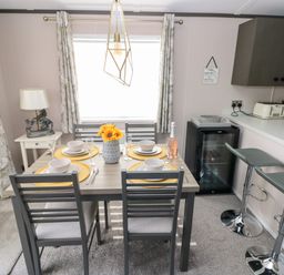 A dining area with a set table and four chairs next to a kitchen counter with two bar stools at Beechwood Lodge Hasguard Cross near Broad Haven