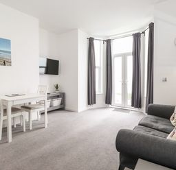 A living room with a gray sofa and coffee table near bay windows with gray curtains and a small dining table with two chairs at 3 Seaview @ Bridlington Bay in Bridlington
