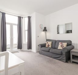 A living room with a gray sofa, floor lamp, wall clock, side tables, white dining table and chairs near windows with gray curtains at 3 Seaview @ Bridlington Bay in Bridlington