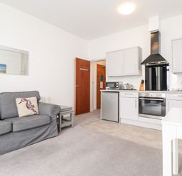 A living room with a grey sofa and pillows near a kitchen with white cabinets a fridge and an oven at 3 Seaview @ Bridlington Bay in Bridlington