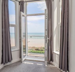 A room with open balcony doors overlooking a beach and sea at 4 Seaview @ Bridlington Bay in Bridlington