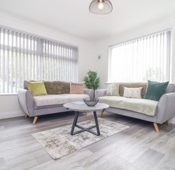 A living room with two sofas, a round coffee table, a small rug, and vertical blinds on windows at Apple Tree Bungalow in Lanner