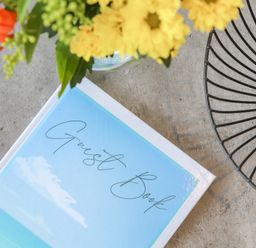 A guest book on a table with a vase of flowers and a decorative wire bowl at Apple Tree Bungalow in Lanner
