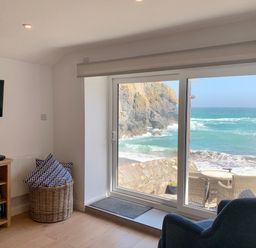 A living room with a window overlooking rocky coastline at Beach Cottage in Cadgwith