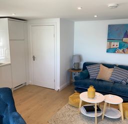 A living room with a sofa, coffee table and kitchen at Beach Cottage in Cadgwith
