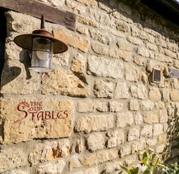 A stone exterior wall with a light fixture and a sign that reads The Old Stables at The Old Stables in Chipping Campden